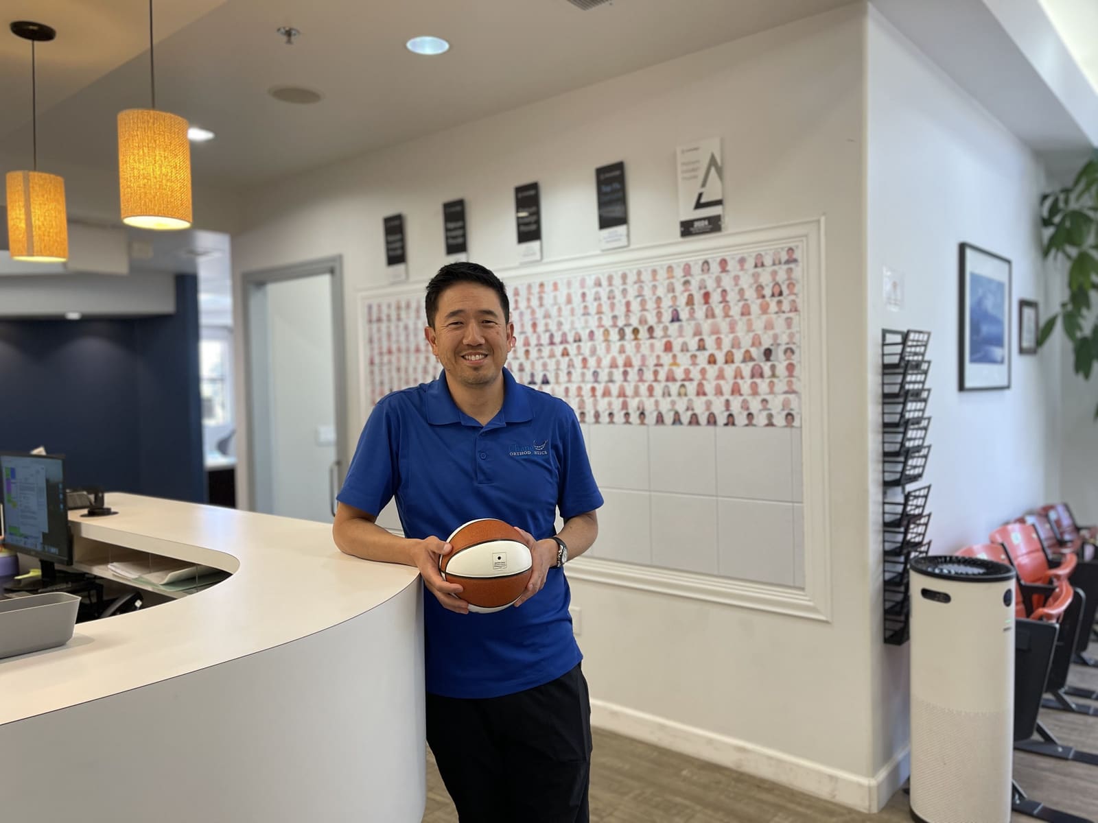 Dr. Chang in the Chang Orthodontics reception area with the patient photo wall