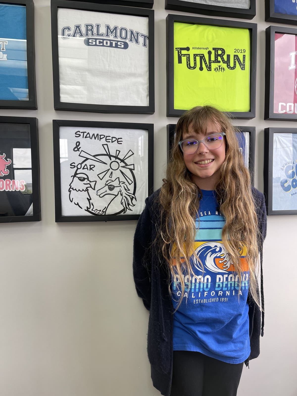 A teen patient smiling in front of the school shirt wall at Chang Orthodontics